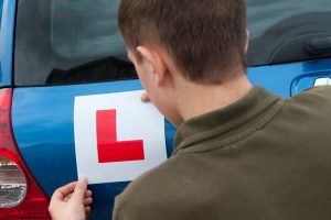 A young person putting an L plate on their blue car