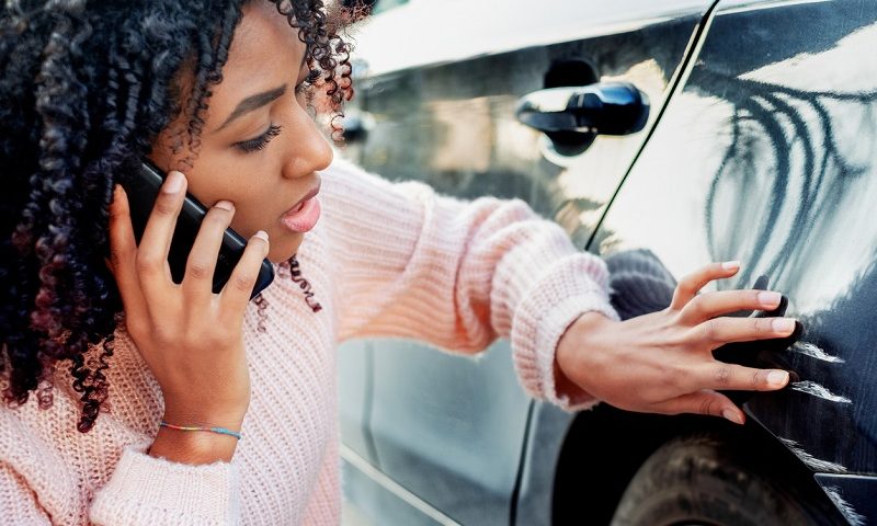 Woman making a phone call while looking at damage on her car