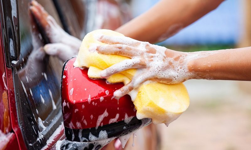 Individual washing red car with sponge and soap