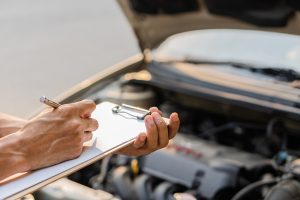 Mechanic checks car engine and writes notes
