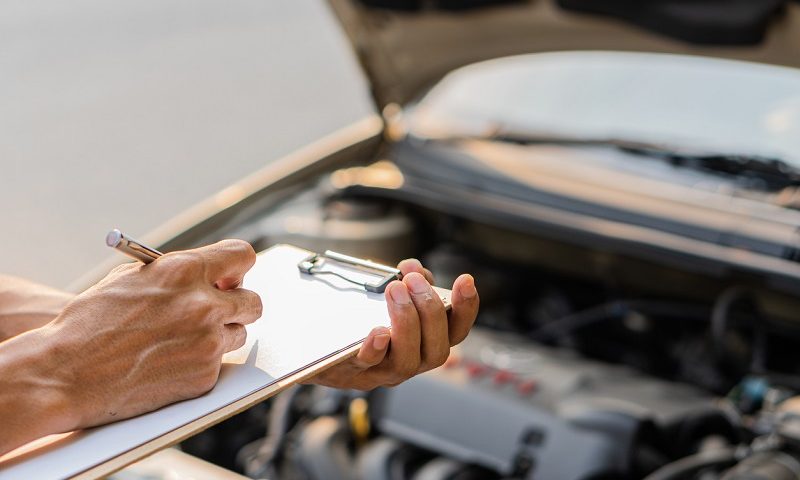 Mechanic checks car engine and writes notes