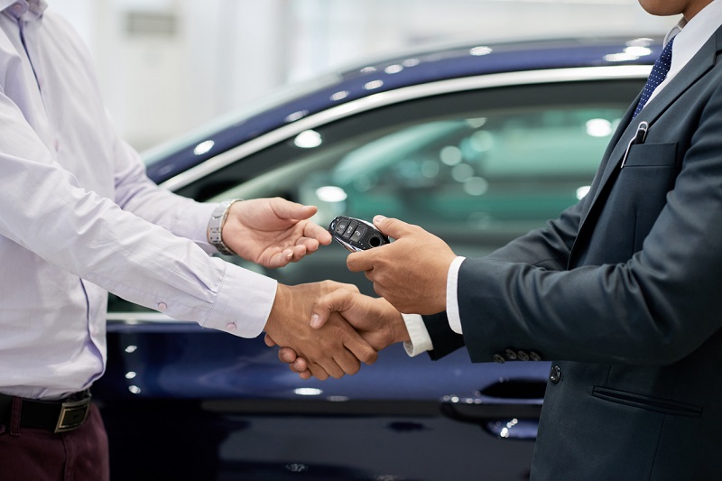 Salesman giving car keys to customer and shaking his hand