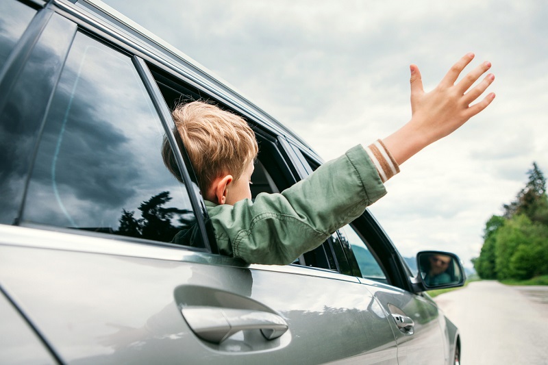 Young boy waving his hand outside a car window