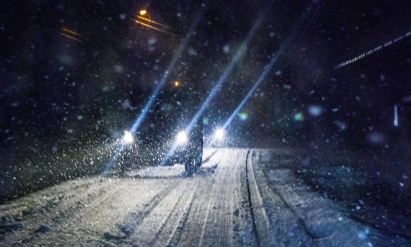 Car driving in the dark during a winter snowstorm.