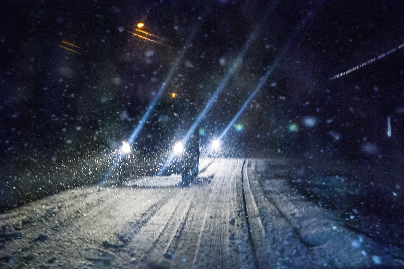 Car driving in the dark during a winter snowstorm.