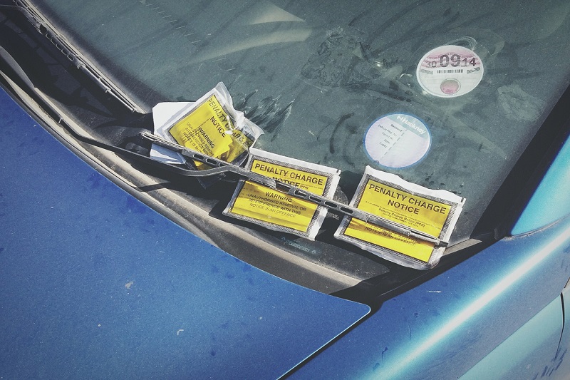 Close up of three parking tickets on the windscreen of a blue car.