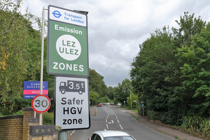 Signs on a British road. One signifies it as part of the ULEZ area, the other says it is a safer HGV zone