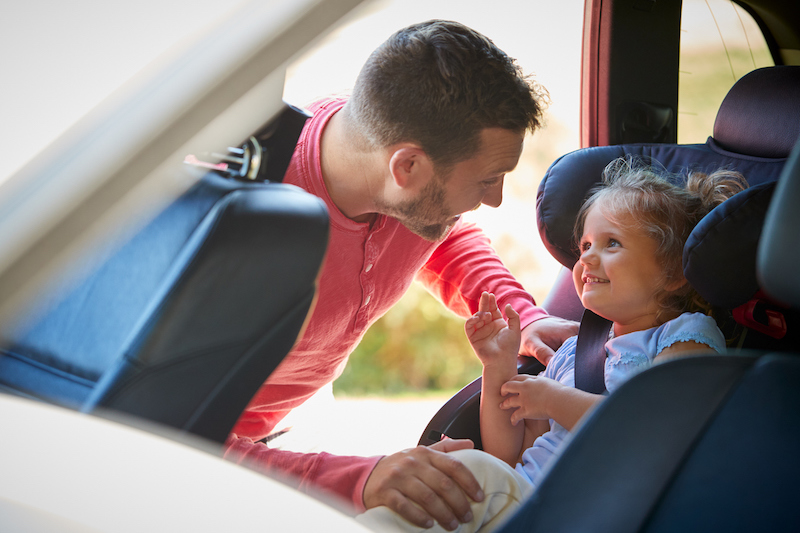 Father securing daughter in rear child seat before road trip