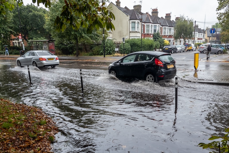 Two cars driving through a large puddle on the road