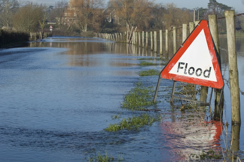 A flood sign next to a flooded road